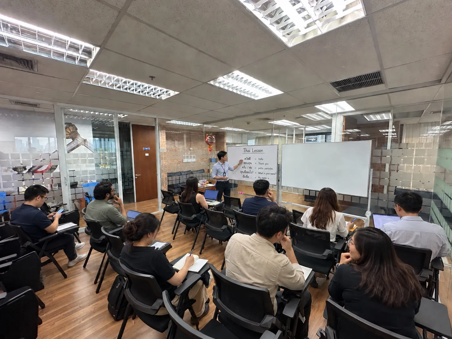 A Thai lesson at the school: the teacher writes greetings and polite particles on the whiteboard for a class of adults