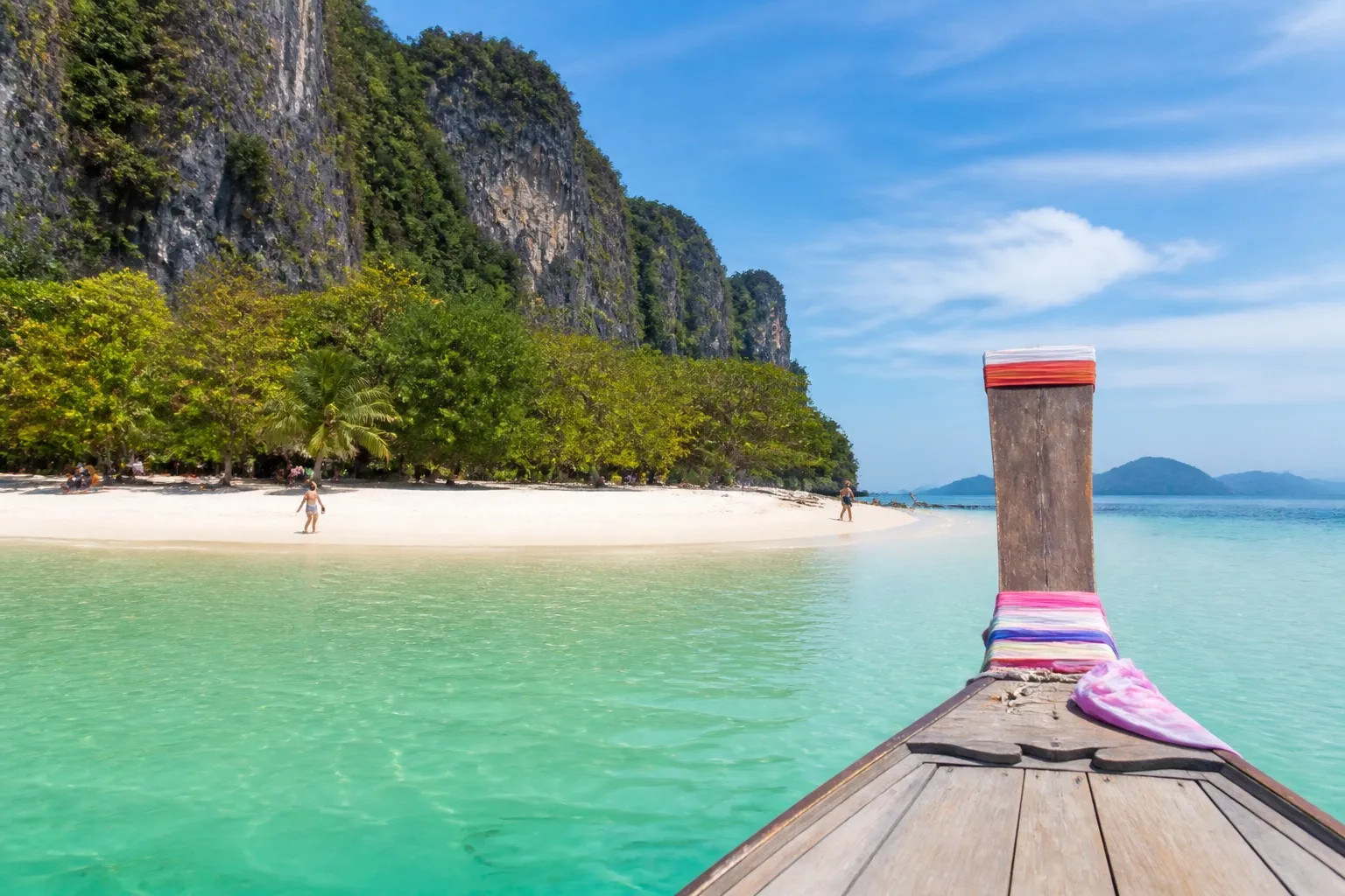 Long-tail boat approaching a quiet tropical Thai island beach