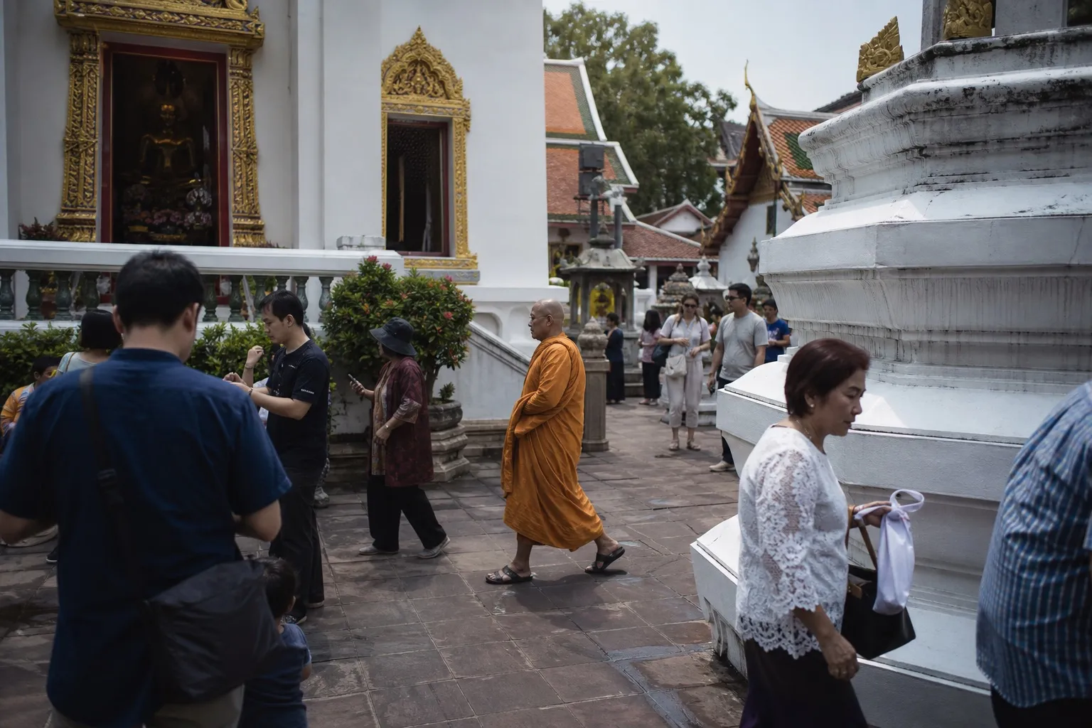 A Buddhist monk and visitors crossing a Bangkok temple courtyard